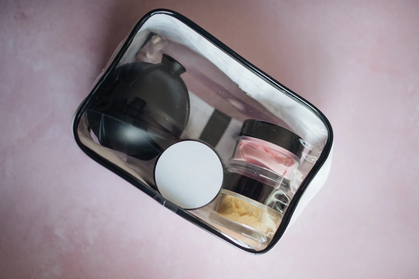 Een doorzichtig toilettasje met kleine cosmeticapotjes en verzorgingsaccessoires.