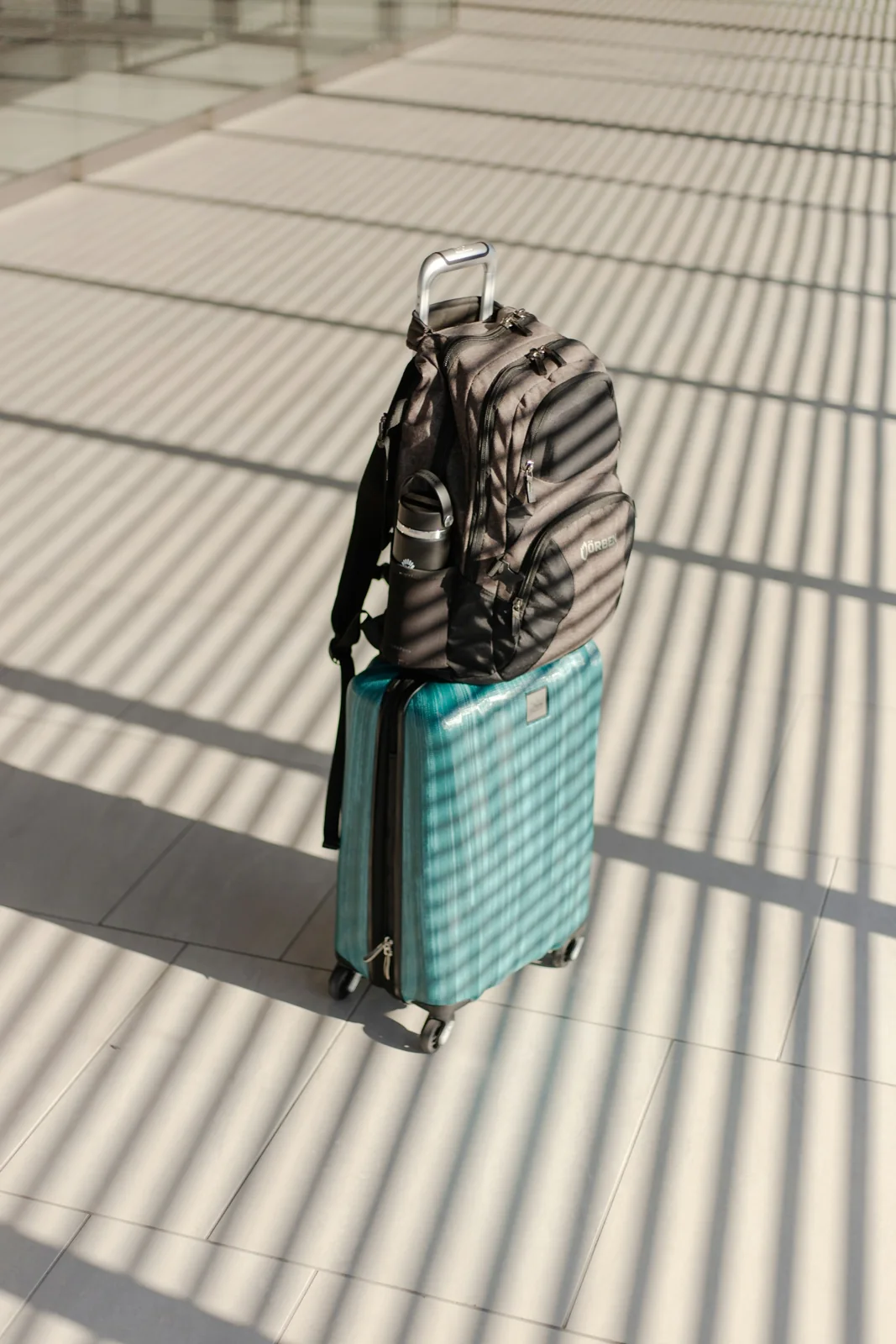 A patterned backpack resting on a turquoise wheeled suitcase.